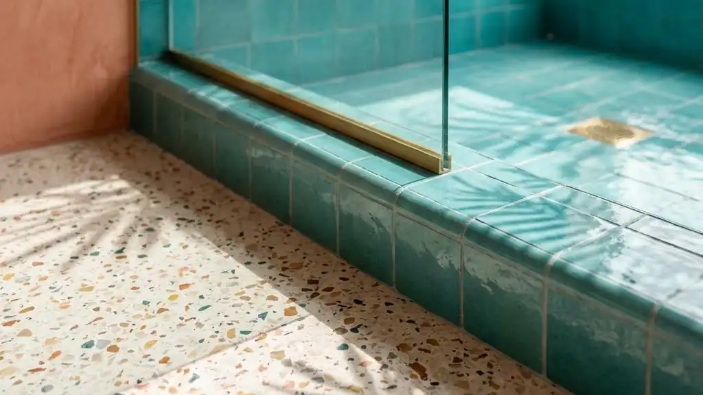 Terrazzo floor meeting a teal tiled shower curb in morning light